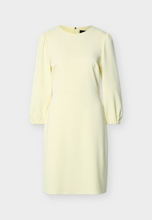Robe jaune pâle jusqu'aux genoux avec manches longues bouffantes, encolure ronde, poignets élastiques et fermeture éclair au dos.