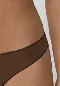 Brązowe bikini o gładkiej fakturze, z niskim stanem i cienkim elastycznym paskiem w talii, podkreślające minimalistyczne detale designu.