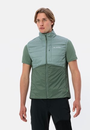 Gilet vert léger sans manches avec deux textures : partie supérieure matelassée, partie inférieure lisse. Caractérisé par une fermeture éclair et un logo sur la poitrine.