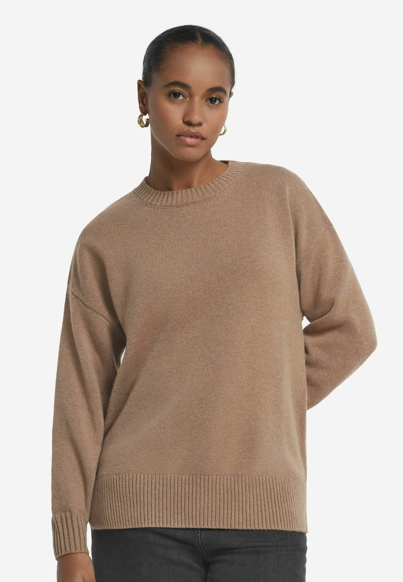 Beiger Strickpullover mit rundem Ausschnitt, gerippten Ärmelbündchen und Saum sowie lässiger Passform. Die Textur wirkt glatt und weich.