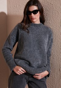 Pull en tricot gris avec un col haut et des poignets côtelés, fait en matière duveteuse. Associé à un jean sombre taille haute.