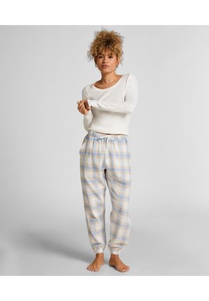 Weißes Langarmoberteil und hellblaue sowie beige karierte Schlafanzughosen mit elastischen Bündchen und Kordelzugbund. Das Modell steht barfuß.