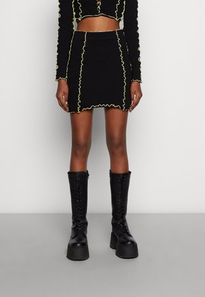 Black ribbed mini skirt with neon yellow wavy trim paired with matching crop top and black platform lace-up boots.
