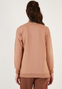 Felpa marrone chiaro con maniche lunghe e polsini a costine. Il retro presenta un design semplice e pulito con scollo rotondo. Tessuto morbido al tatto.