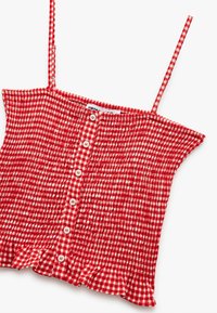 Rood en wit geblokt mouwloos topje met een gerimpelde onderrand, voorzien van kleine knopen en een geplooide textuur overal.