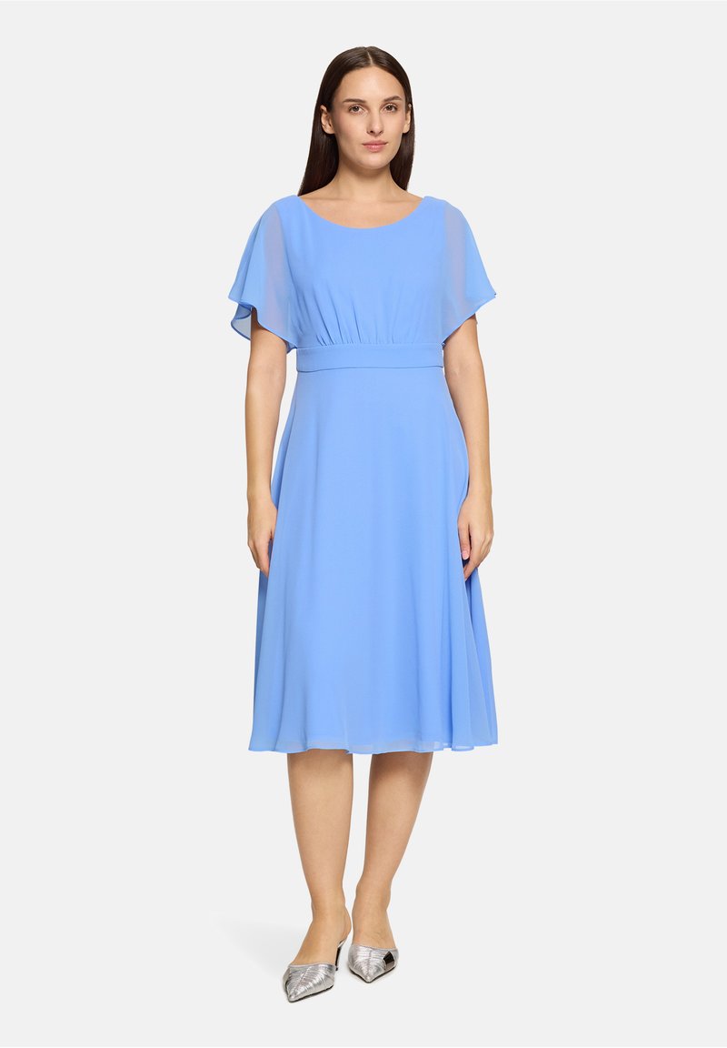 Hellblaues, knielanges Kleid mit kurzen, fließenden Ärmeln und tailliertem Schnitt. Glatter Stoff und weiche Textur. Kombiniert mit silbernen spitzen Ballerinas.