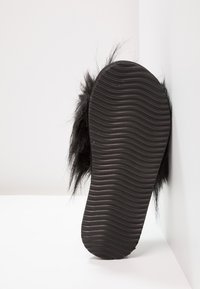 Black fur-lined slide sandal with a textured rubber sole. The underside features prominent wavy grooves for traction.