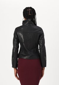Crna kožna jakna s pripijenim dizajnom, visokim ovratnikom i patentnim zatvaračima na rukavima. Glatka tekstura s minimalnim šavovima, nosi se preko rebrastog bordo suknje.