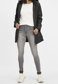 Czarna wodoodporna kurtka z kapturem, zestawiona z lekkim swetrem, szarymi jeansami slim fit i białymi trampkami z żółtymi akcentami.