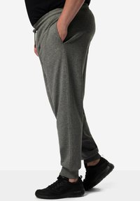Grijze sweats met een trekkoord in de taille, taps toelopende benen, zijzakken en een subtiel logo op de dij. Gepaard met zwarte sport schoenen.