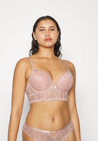 Sutiã rendado em rosa suave com padrão floral, bordas em scallop e suporte de arame. Alças ajustáveis e um detalhe de buraco na parte central.