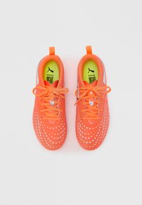 Zapatillas deportivas de un naranja brillante con una parte superior texturizada, patrones de flores blancas y plantillas de neón verde. Cordones y tiradores a juego en naranja.