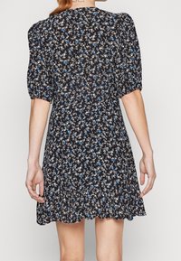 Robe noire à fleurs avec des motifs bleus et blancs, manches bouffantes, taille cintrée et ourlet festonné. Tissu léger, design décontracté.