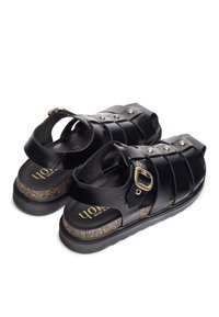 Sandalias de cuero negro con múltiples correas y herrajes en tono dorado. Suela texturizada tipo corcho que proporciona amortiguación. Diseño abierto para transpirabilidad.