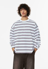 Langärmliges gestreiftes Hemd in Weiß, mit horizontalen Streifen in Marineblau, Rot und Schwarz. Aus Baumwollmaterial mit lockerer Passform und rundem Ausschnitt.