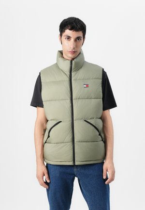 Padded vest in light olive green, with a high collar, front zipper, and black accents. Features side pockets and a small logo on the chest.