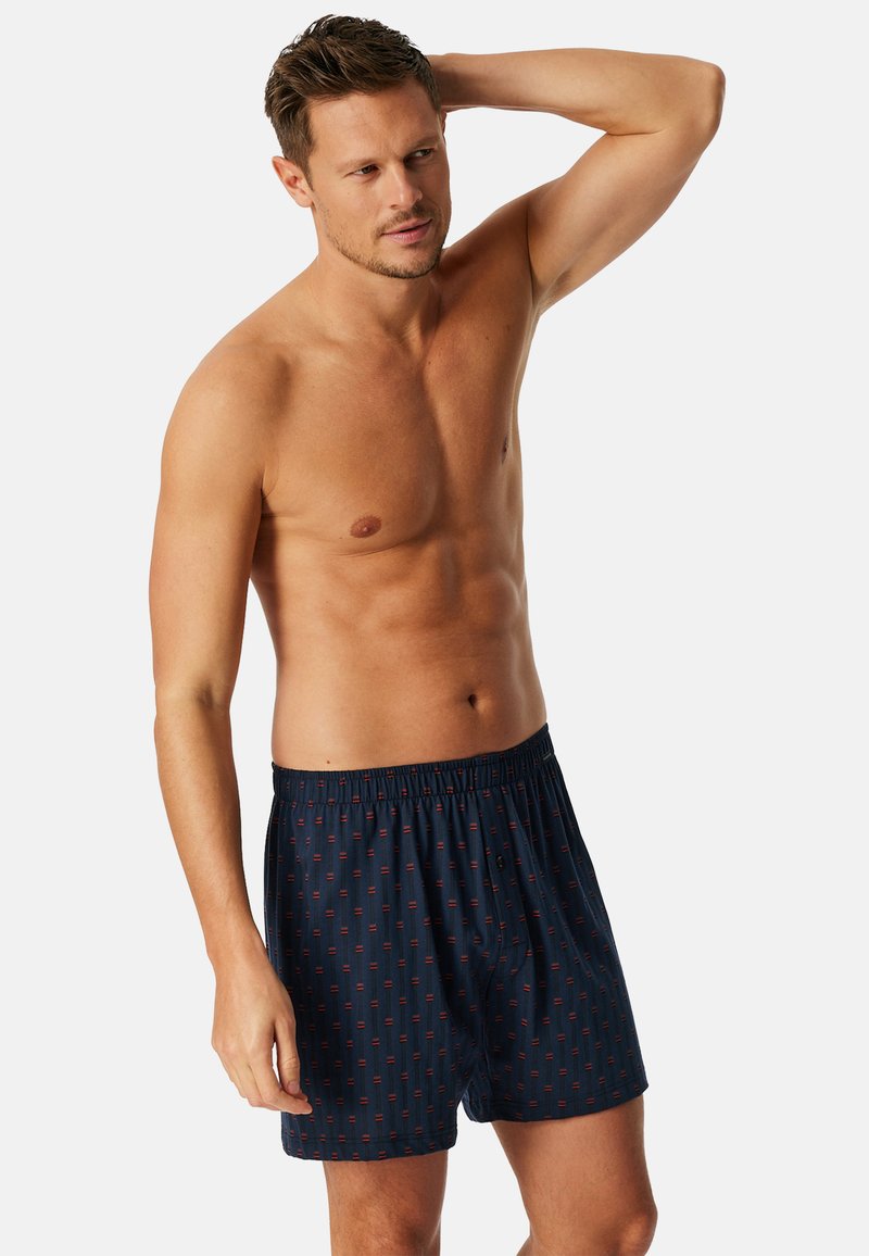 Marineblauwe boxers met een geometrisch rood patroon, elastische tailleband, lichtgewicht stof en een relaxte pasvorm.