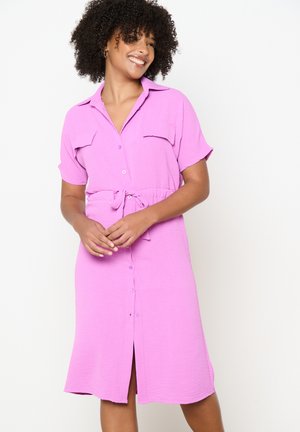 Abito rosa con bottoni, maniche corte, due tasche sul petto e vita legata. Tessuto a trama, forma svasata e lunghezza al ginocchio.