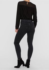 Jeans skinny de tiro alto negros con una textura suave, que cuentan con bolsillos traseros y se llevan con botas negras de tobillo.