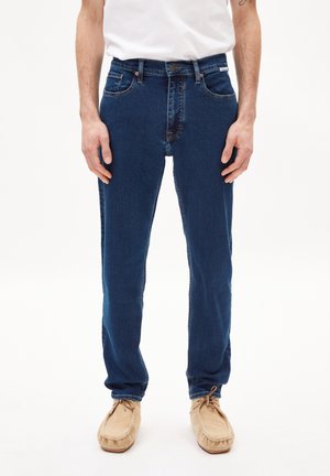 Dunkelblaue Denim-Jeans mit schlanker Passform, Fünf-Taschen-Design, sichtbaren Steppnähten und einem dezenten, ausgewaschenen Bereich an der Vorderseite.