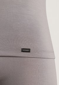 Top grigio a canotta con una texture liscia, un design aderente e un piccolo etichetta nera con "HANRO" cucita sul lato inferiore della cucitura.