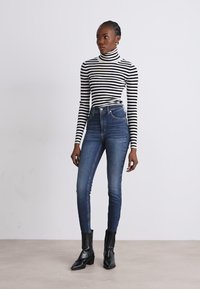 Raitapaita, jossa on korkeakaulukset, musta-valkoisena; korkeavyötäröiset siniset farkut; mustat nilkkurit; slim fit; sileä tekstuuri; minimalistinen muotoilu.