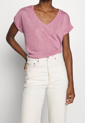 Top rosa in lino a maniche corte con scollo a V, abbinato a jeans bianchi a vita alta con chiusura a quattro bottoni e tasche laterali.
