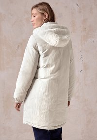 Lichtgrijze gewatteerde jas met een zachte, crèmekleurige fleece-voering in de capuchon, geribbelde manchetten en een middellange snit. Textuurstof overal.