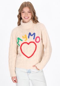 Cremfarbener Strickpullover mit hohem Kragen, der bunte Filzbuchstaben und ein rotes Herzdesign auf der Vorderseite zeigt.