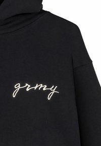 Sudadera negra con una textura suave y un corte relajado. Presenta un bordado en cursiva blanca que dice "grmy" en el frente.
