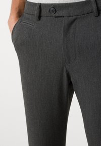 Grijze broek gemaakt van gestructureerde stof, met een platte voorkant, steekzakken aan de zijkant en een sluiting met één knoop. Gedetailleerde stiksels zijn zichtbaar.