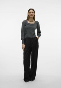 Grauer Strickpullover mit langen Ärmeln und quadratischem Ausschnitt, kombiniert mit hochgeschnittenen, schwarzen, weit geschnittenen Hosen. Eine klobige silberne Halskette rundet das Outfit ab.