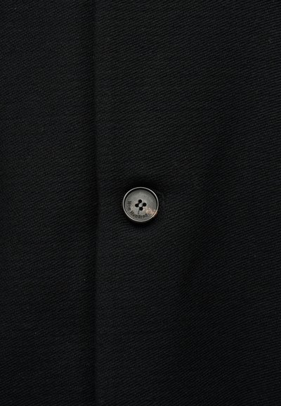 Μαύρο ύφασμα με ένα κουμπί τεσσάρων τρυπών ραμμένο στο κέντρο, το κουμπί είναι χαραγμένο με το κείμενο «Won Hundred».