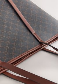 Sac en similicuir marron à motifs, avec une surface grise texturée, doté de longues lanières marron et d'un motif géométrique répétitif.