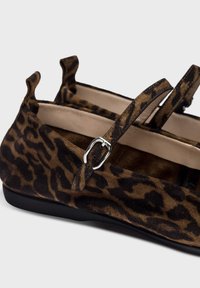 Chaussures plates en suède imprimé léopard, dotées d'une semelle noire et d'une sangle décorative avec une boucle en argent. Surface douce et texturée.