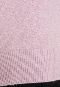 Pull rose clair en tricot, doté d'un ourlet côtelé et d'une texture douce, vue en gros plan mettant en valeur le tissage uniforme du tissu.