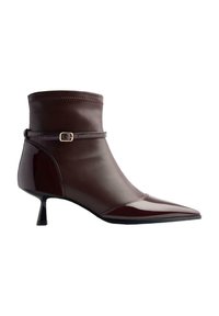 Bottine en cuir marron avec un bout pointu, un petit talon kitten, et une fine sangle avec une petite boucle en or autour de la cheville.