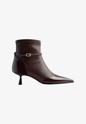 Stivaletto in pelle marrone con punta affusolata, tacco kitten piccolo e una sottile cinghia con una piccola fibbia dorata attorno alla caviglia.