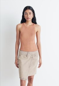 Top a coste senza maniche di colore arancione bruciato, abbinato a una gonna di jeans asimmetrica beige con chiusura a bottone e zip.