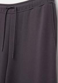 Pantalon de survêtement gris foncé avec taille élastique et cordon de serrage, gros plan montrant la texture lisse du tissu et les coutures sur le côté.