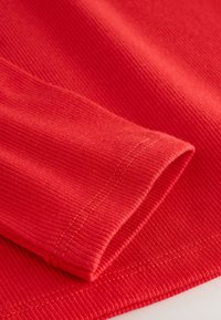 Red ribbed fabric with a smooth texture, featuring a rolled cuff and visible stitching in a contrasting shade.