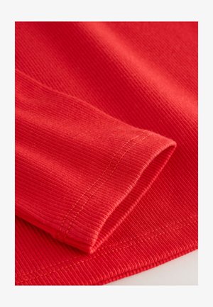 Tessuto a costine rosso con una texture liscia, caratterizzato da un risvolto arrotolato e cuciture visibili in una tonalità a contrasto.