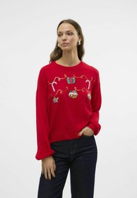 Maglione rosso con decorazioni festive ricamate, tra cui regali, bastoncini di zucchero e ornamenti, con polsini a coste e una texture morbida.