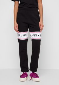 Svarta sweatpants med vita och rosa accentband som har ögon- och stjärnmönster, elastisk midja och tapered bendesign.