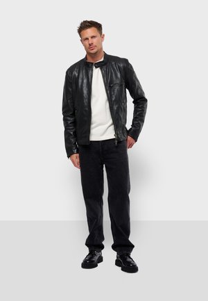 Schwarze Lederjacke mit Stehkragen, Reißverschluss-Tasche, cremefarbenem Sweatshirt darunter, schwarzen Jeans und schwarzen Schuhen. Einfaches Design, glatte Textur.