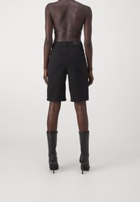 Černé denimové šortky s rovnými nohavicemi a zadními kapsami, doplněné černými koženými vysokými botami na podpatku.