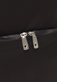 Zwarte stoffen tas met dubbele zilveren metalen ritsen met gegraveerd logo. Glad textuur met een strakke vormgeving en minimalistische accenten.