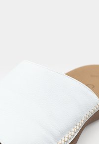 Bílé kožené skluzné sandály s texturovaným svrškem, prošívanými detaily a hladkou opalovací stélkou. Design je minimalistický a moderní.