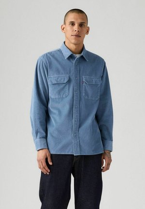Camisa de pana azul claro con mangas largas, dos bolsillos en el pecho, cierre de botones y una etiqueta de Levi's en el bolsillo izquierdo.