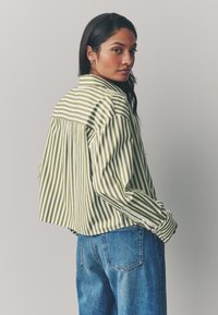 Maglietta a righe verdi e bianche con vestibilità ampia, spalle scese e pieghe sul retro, abbinata a jeans di denim blu.